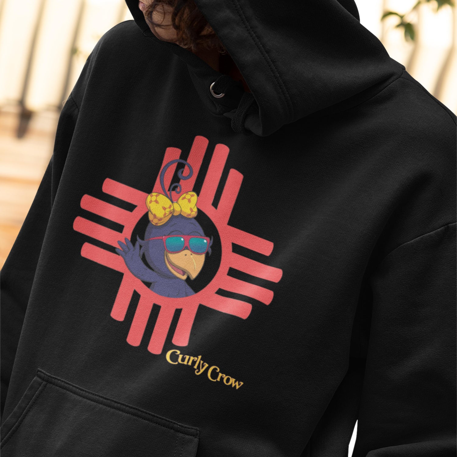 Curly Crow T-shirt with bold New Mexico Zia symbol, featuring Curly waving from the center. Available in kids and adult unisex sizes. Hand-printed, Southwest-themed apparel.