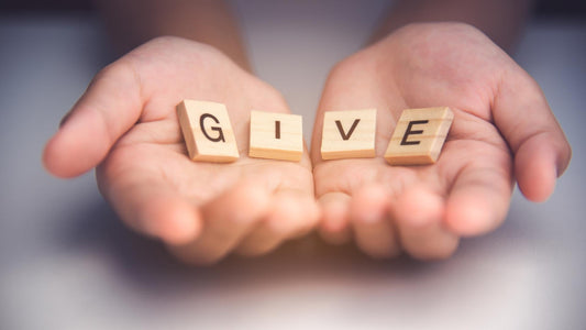 Human hands holding letters that say "Give" to remind us that others are in need of books, give with the Curly Crow Book Donation Program