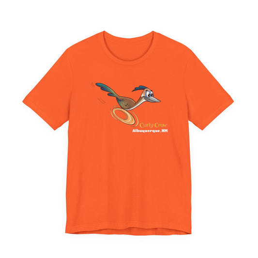 A orange short-sleeve crewneck t-shirt featuring a Curly Crow cartoon graphic of the New Mexican roadrunner.