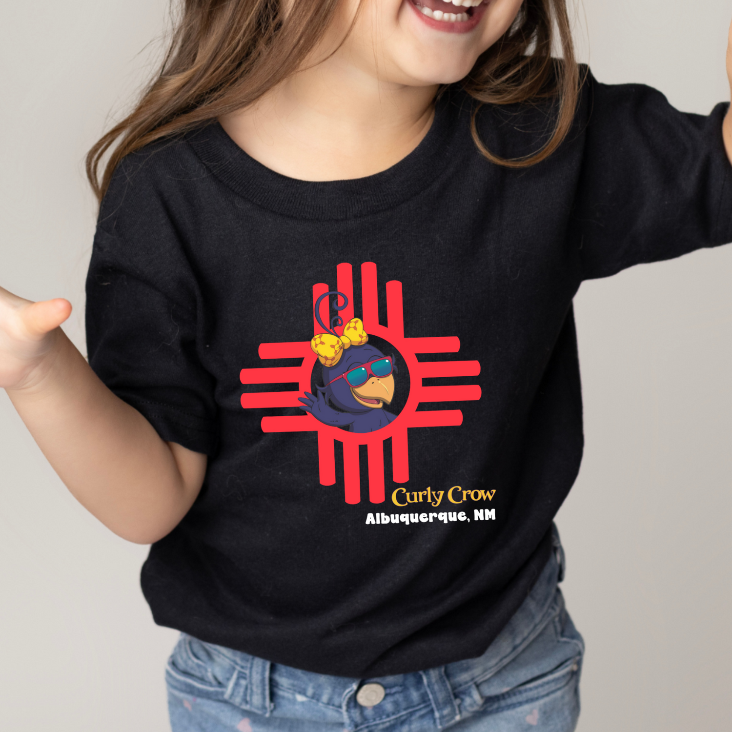 Child wearing a black t-shirt with a red NM Zia graphic design with Curly Crow on a plain background
