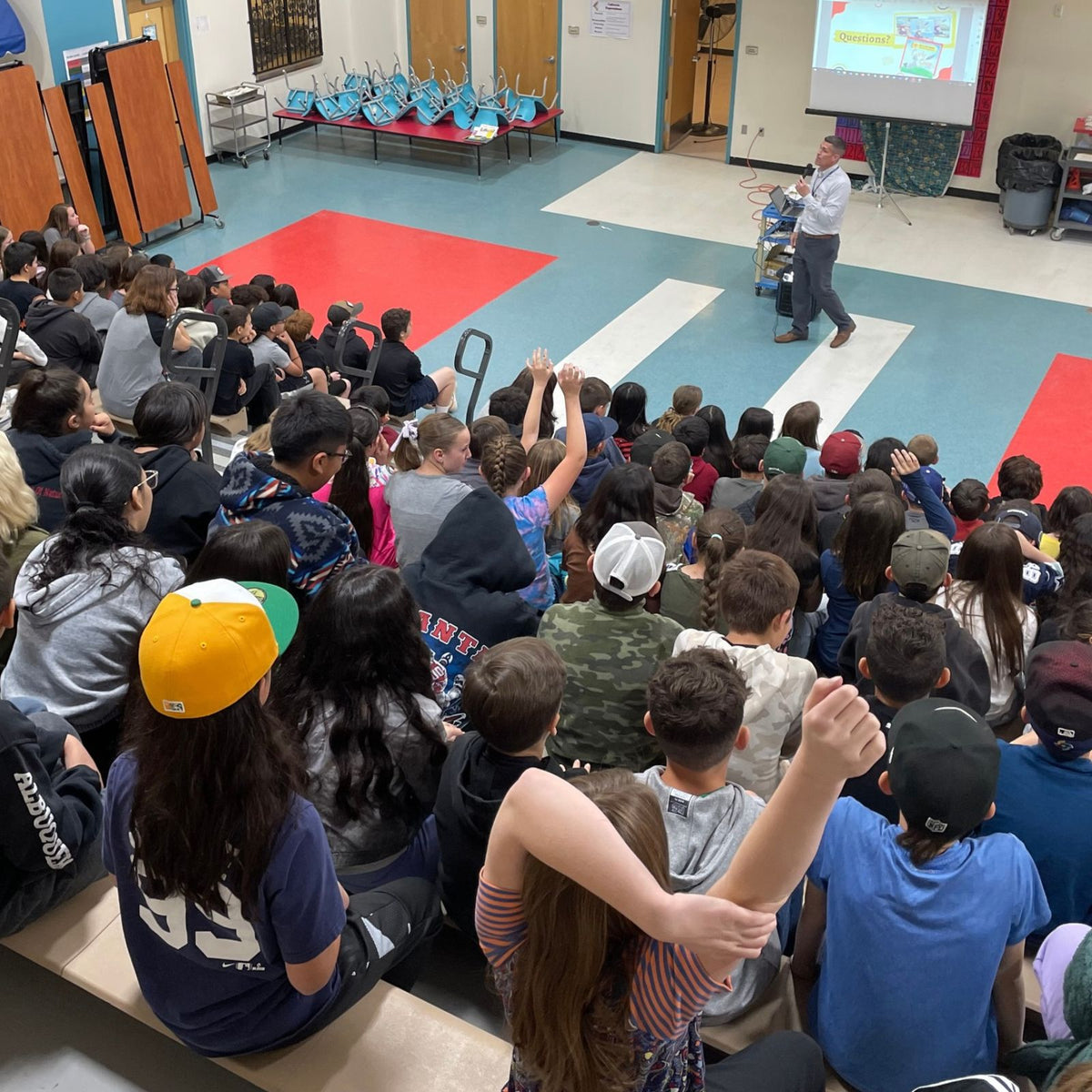 Author Nicholas Aragon speaking in front of a large crowd of elementary school students and teachers. 